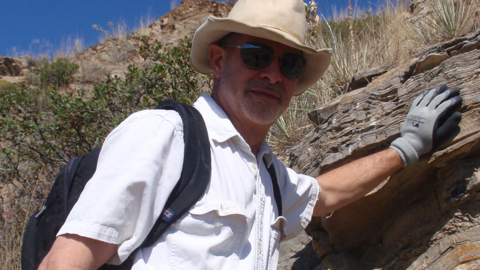 Robert M. Hazen places his gloved hand on a rock face.