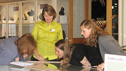 4 educators examine specimen in mineral hall. 
