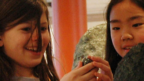 two smiling girls handle small object.