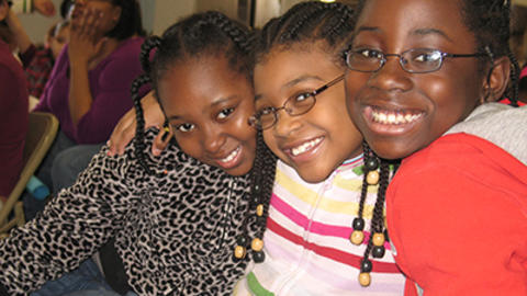 3 girls smile for camera and hold each other close.