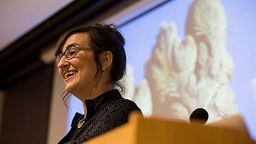 Woman at podium with slideshow in the background discussing her research.