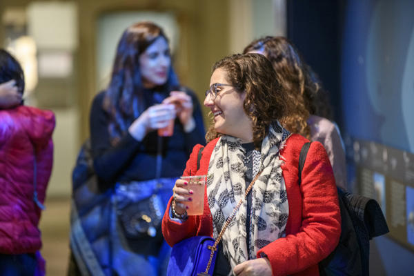 Woman with a red jacket drinking a beverage in the galleries.