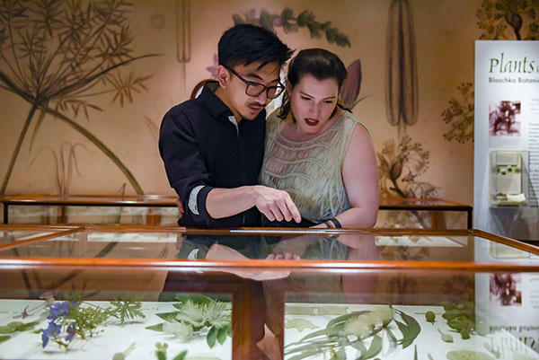 A woman and a man closely looking at a glass flower model.