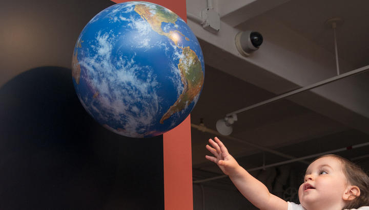Young girl reaching towards a model Earth.