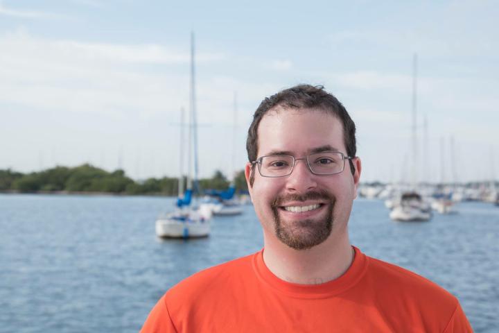 Speaker, Dr. David Shiffman, outside smiling with water and boats behind him.