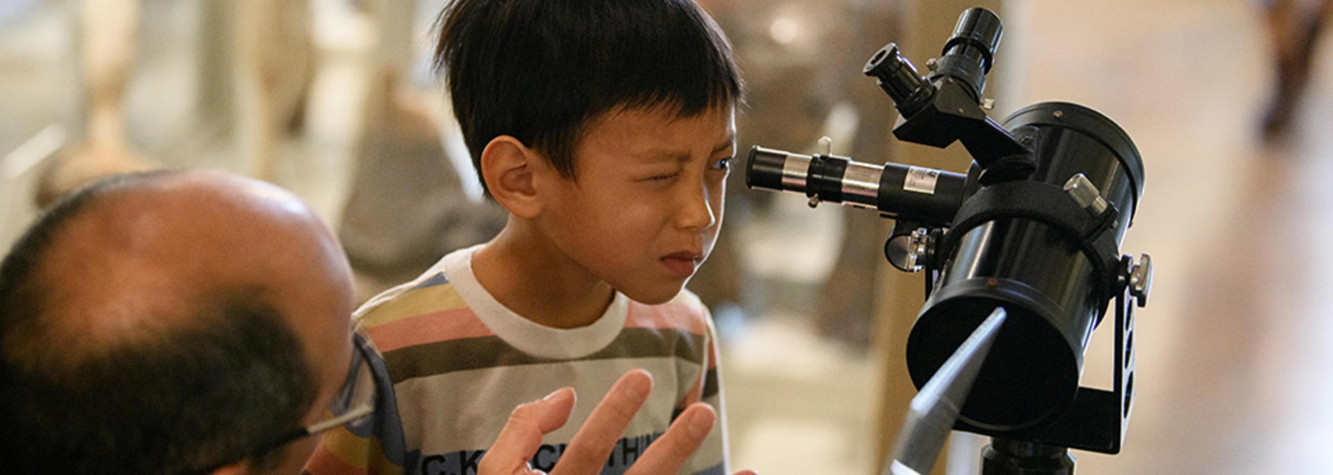 man helps boy squint through telescope.