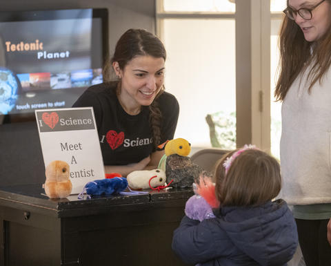 A scientist engages in discussion with a young patron over a table.