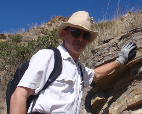 Robert M. Hazen places his gloved hand on a rock face.